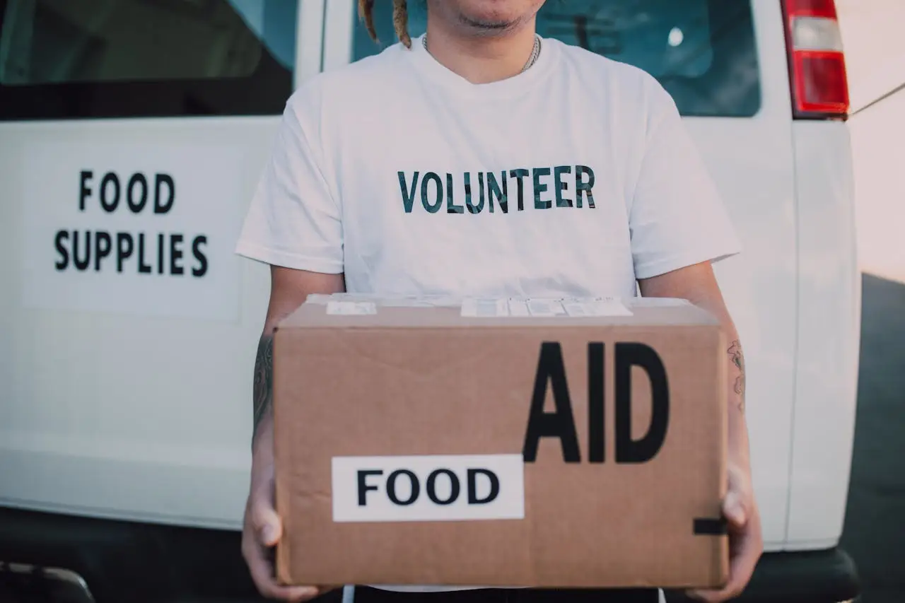 A volunteer holding a food aid box in front of a supply vehicle, ready for distribution.